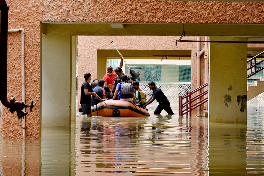 A man pushes a boat filled with people away from stairs in floodwaters.