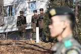 Three North Korean Soldiers stand in front of a building at the demilitarised zone looking towards a South Korean soldier