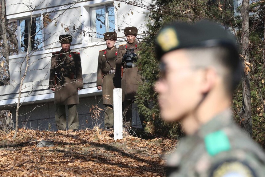 North Korean Soldiers stand at the demilitarised zone looking towards a South Korean soldier.