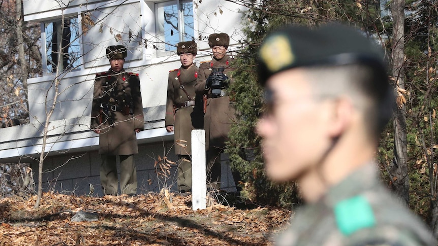 Three North Korean Soldiers stand in front of a building at the demilitarised zone looking towards a South Korean soldier
