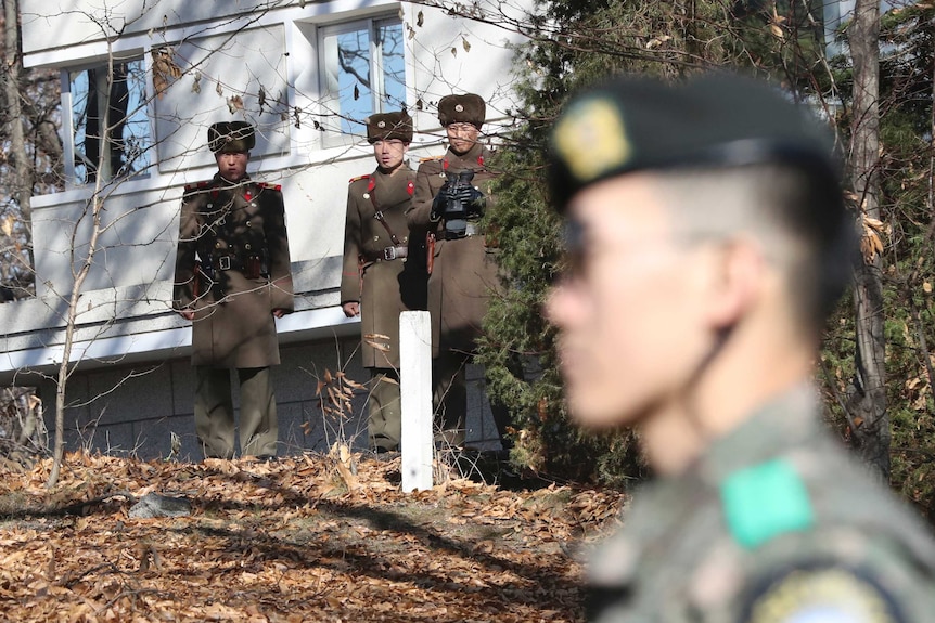 North Korean Soldiers stand at the demilitarised zone looking towards a South Korean soldier.