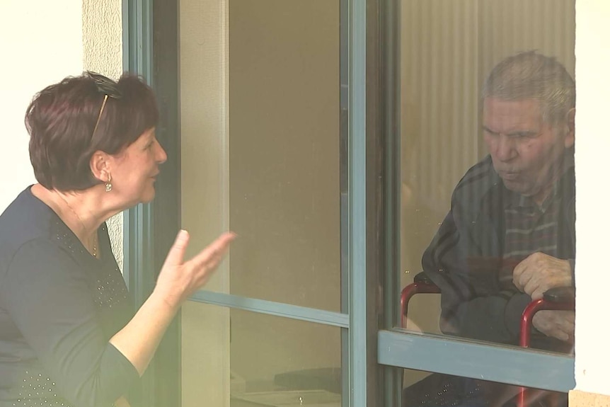 A woman speaking to an elderly man behind a window