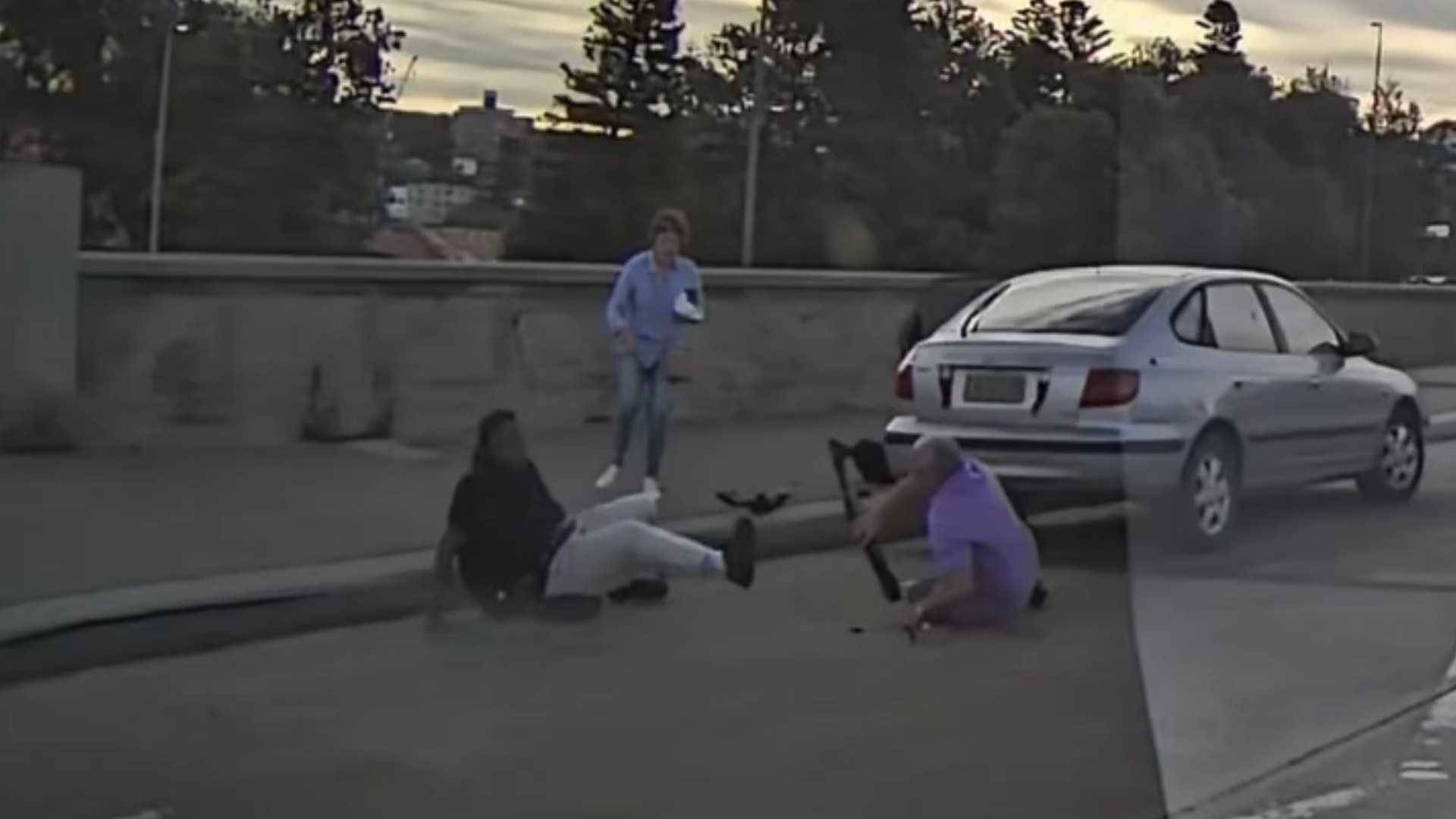 Um homem de camisa roxa é visto segurando a arma de fogo enquanto o atirador cai no chão.