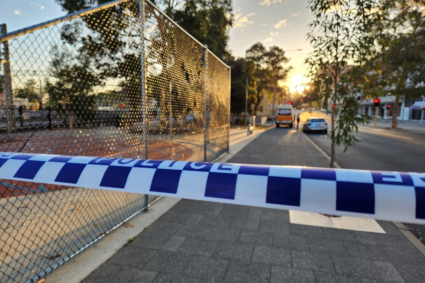 A close-up shot of police tape across a footpath in Perth's CBD with a road and buildings in the background.