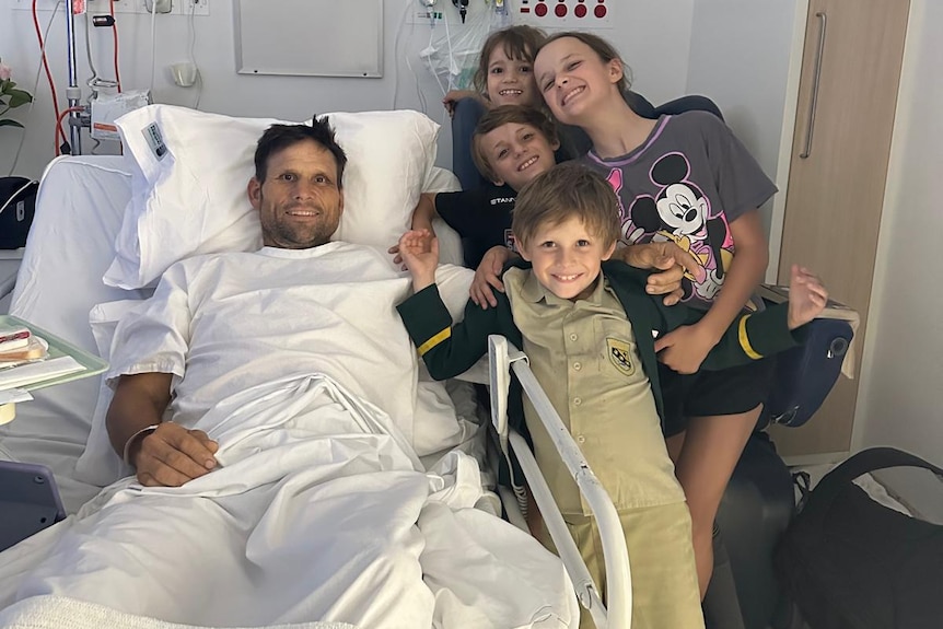 A man in hospital with his children by his bedside.