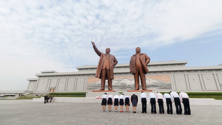 Workers bow before statues of Kim Il-sung and Kim Jong-il at a monument in Pyongyang.