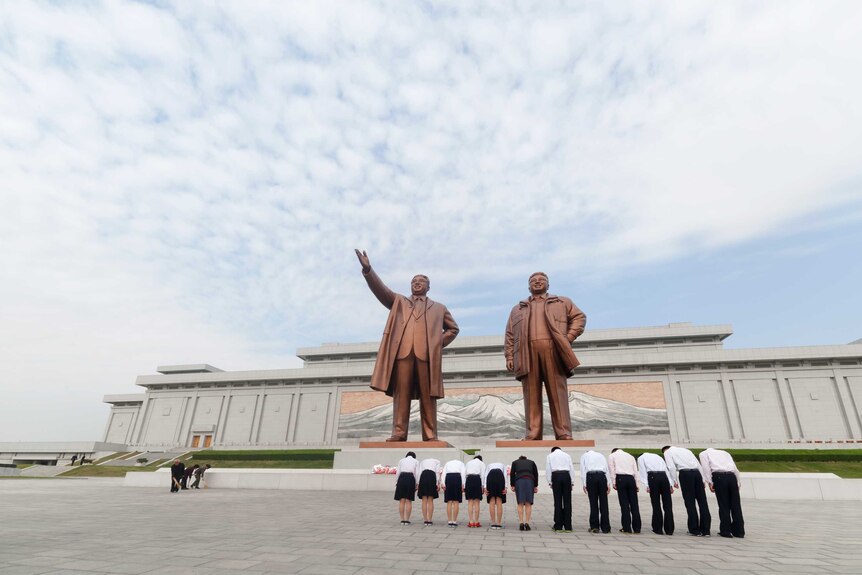 Workers bow before statues of Kim Il-sung and Kim Jong-il at a monument in Pyongyang.