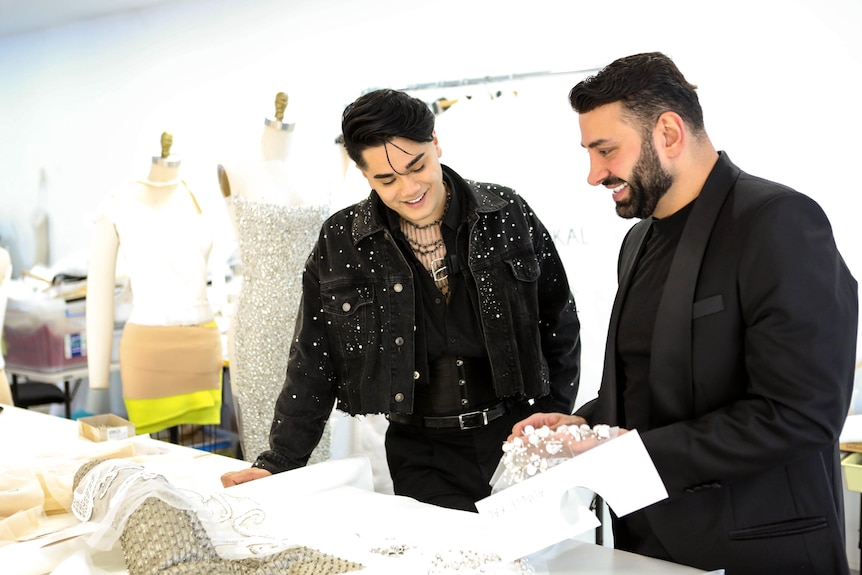 Australia's Eurovision performer Sheldon Riley and designer Alin Le'Kal smile as they look at fabric on a table.