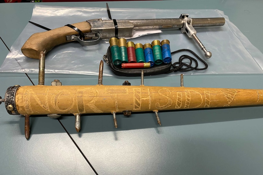 A table with a small gun, shotgun shells and a wooden baseball bat with spikes