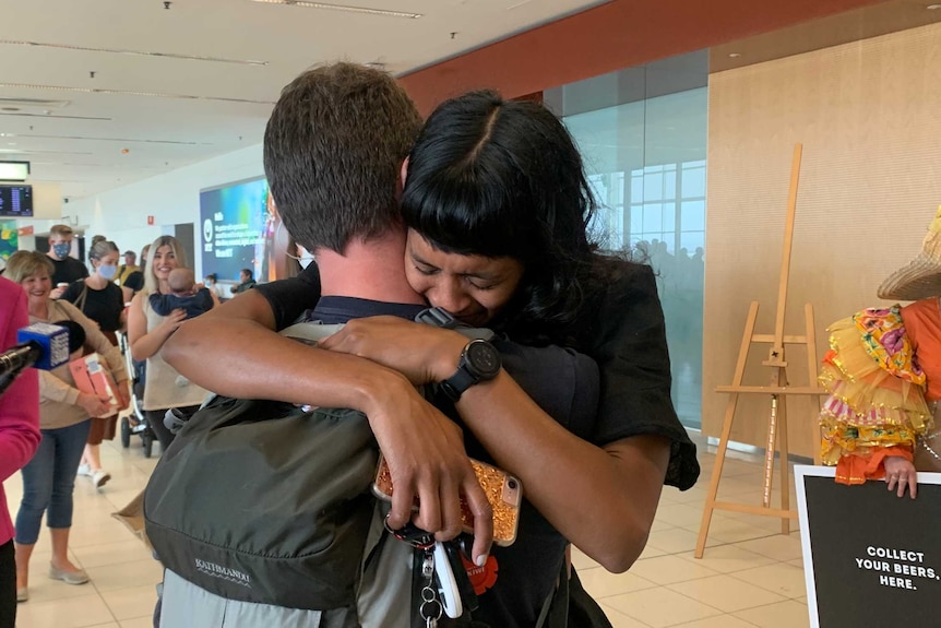 A man and a woman embrace in an airport.