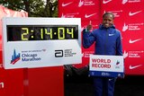 A female runner gives a thumbs up as she stands next to a clock with her world record marathon time.