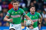 A Canberra Raiders NRL player holds the ball in his left hand as he beats a Melbourne Storm defender.