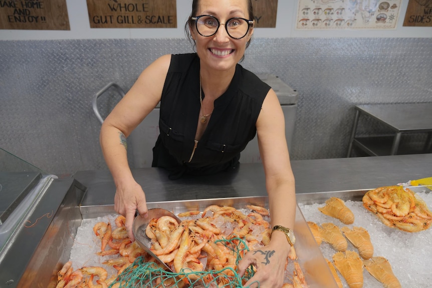 a middle aged woman smiles while scooping prawns