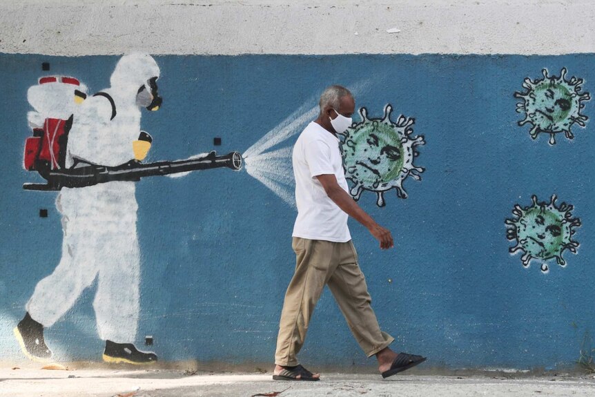 A man walks next to a graffiti depciting a cleaner wearing protective gear spraying viruses with the face of Brazil's President
