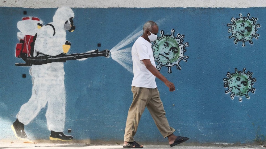 A man walks next to a graffiti depciting a cleaner wearing protective gear spraying viruses with the face of Brazil's President