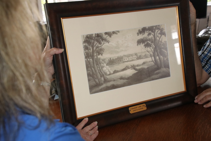 A woman holds a framed sketch of an old house