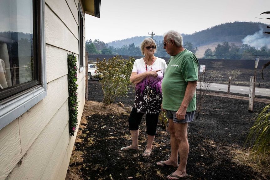 A couple standing on scorched land in front of a home.