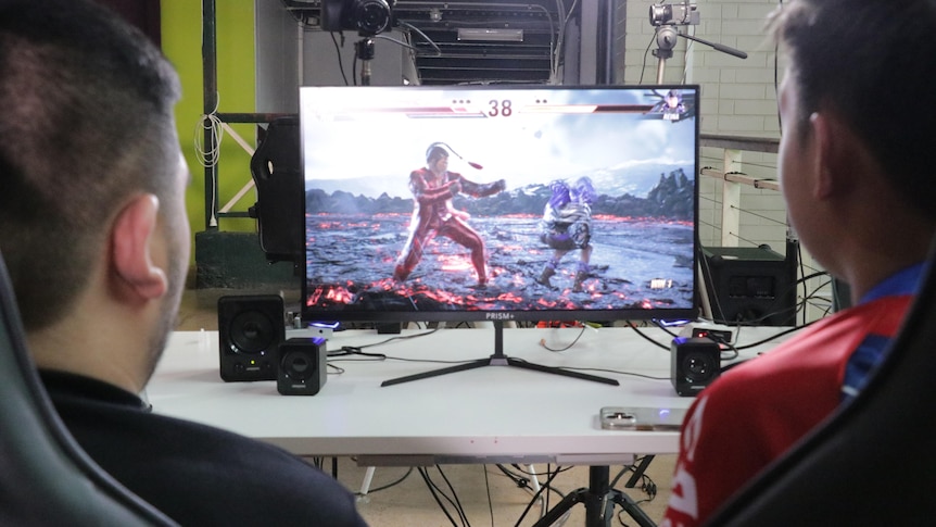 A computer monitor displaying Tekken, with two people out of focus looking at the screen.
