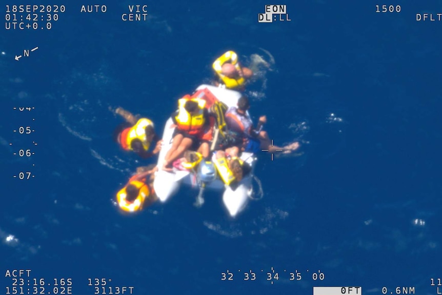 People in life jackets floating in the water and clinging to a small boat