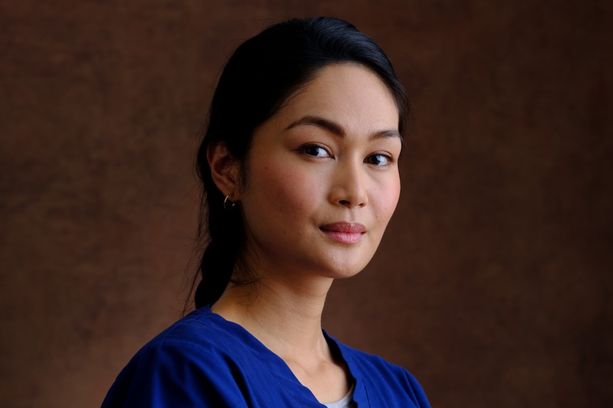 A woman of Filipino heritage smiling wearing nurse scrubs.
