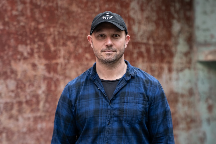 Man wearing a hat and blue check shirt serious expressions down the barrel