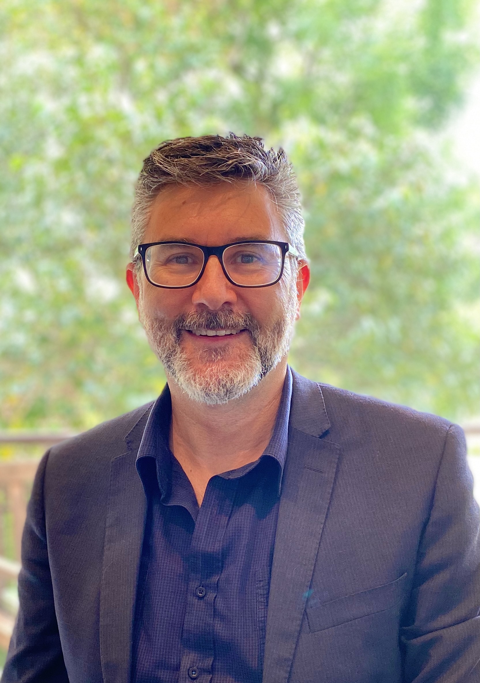 A man in glasses and suit smiles at camera.