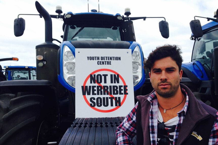 Ricky Santamaria stands with his tractor and a sign that says "youth detention centre not at Werribee south".