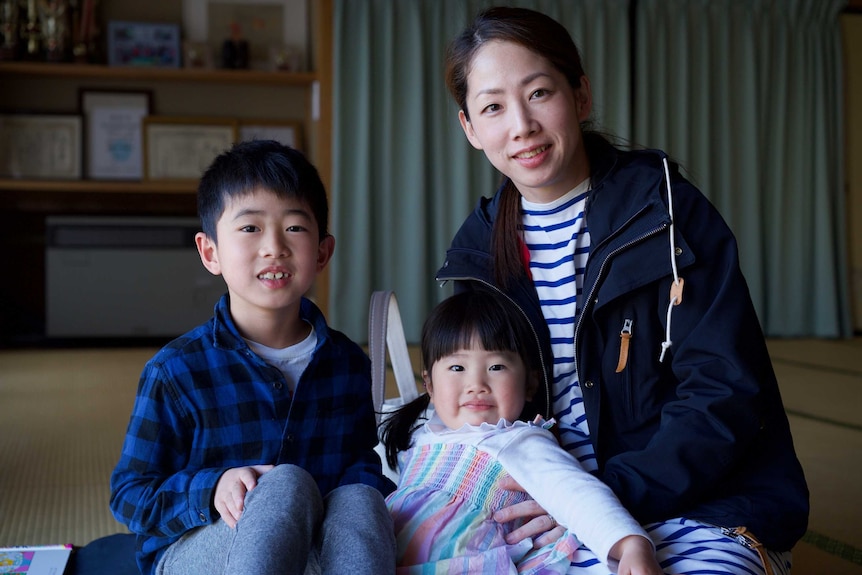 A Japanese woman sits on the floor with her seven-year-old son and three-year-old daughter