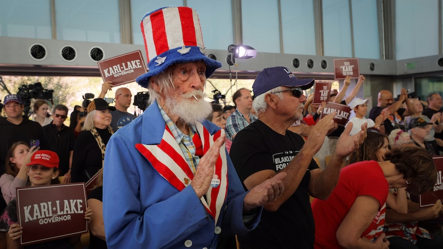 A bearded man in an Uncle Sam costume applauds in a crowd 