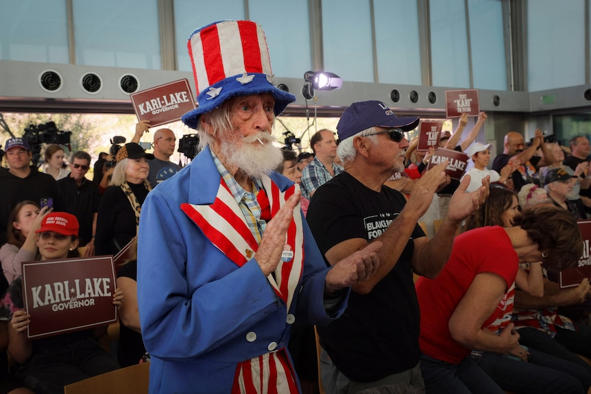 A bearded man in an Uncle Sam costume applauds in a crowd 