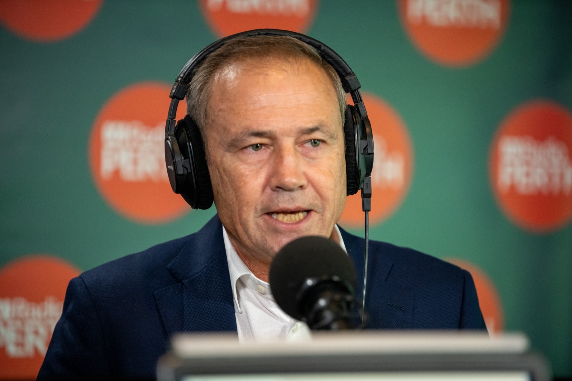 Um close da cabeça e dos ombros do primeiro-ministro de WA, Roger Cook, falando em um estúdio de rádio com fones de ouvido durante uma entrevista.