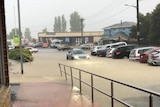 A flooded street in a town showing parked cars sitting in water and a car driving through floodwater.