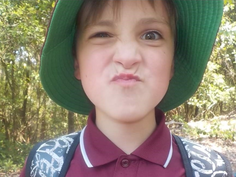 A young boy wearing a hat and school uniform is pulling a face at the camera.