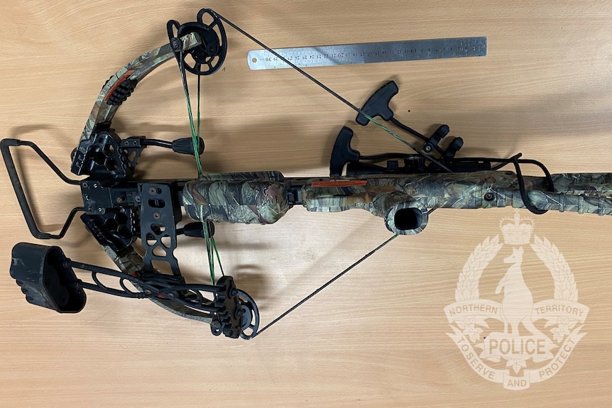 A green camouflage crossbow on a wooden desk, an NT Police watermark over the photo.