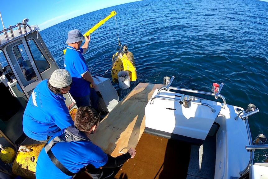 Three people winch a yellow seismometer into a boat.