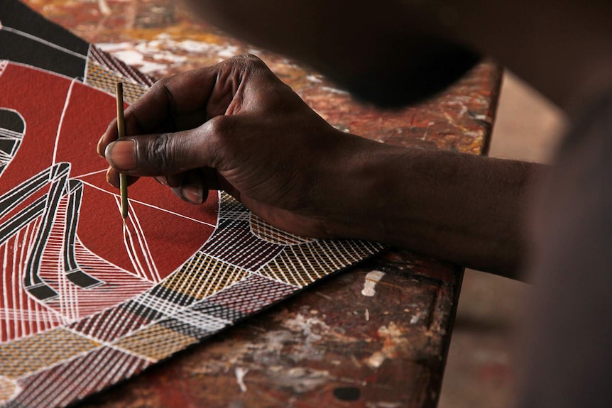 A photo of artist Isaac Girrabul's hand as he paints using a bamboo reed.