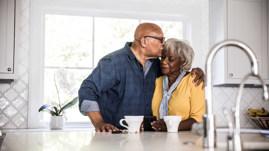 A man and woman embrace in their kitchen.