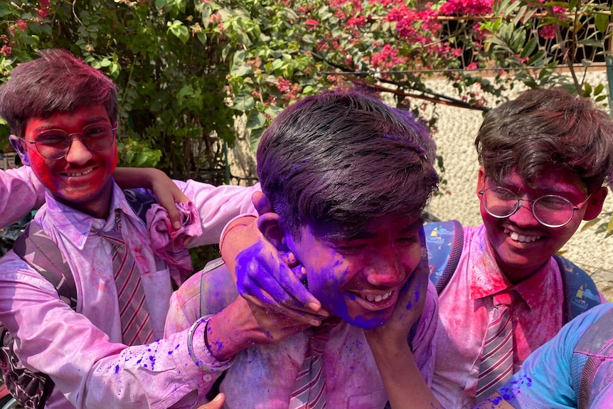 three boys smile covered in pink and purple powder