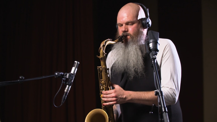 Adam Page plays saxophone wearing headphones.