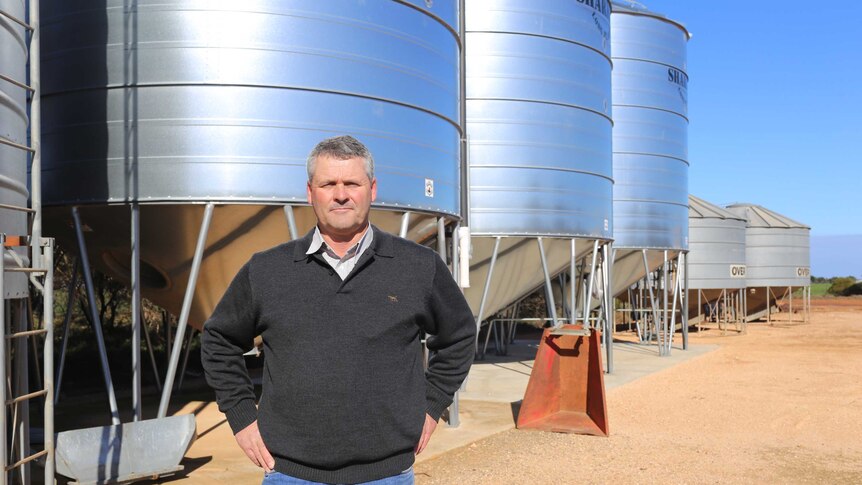 A farmer stands in front of silos.