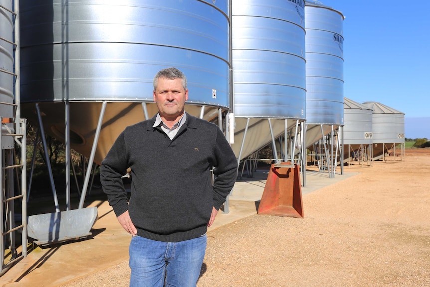 A farmer stands in front of silos.