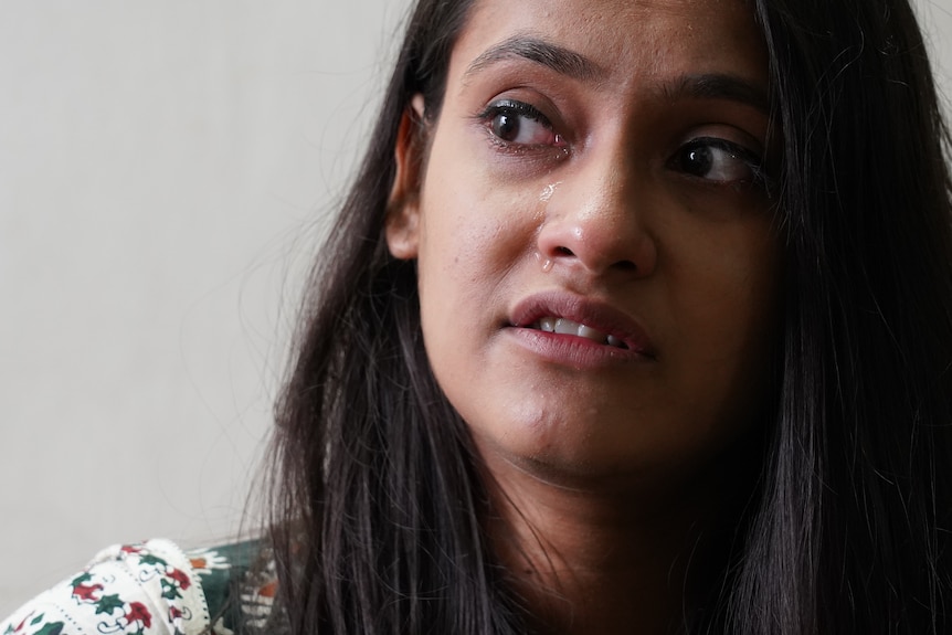 A young Indian woman looking off camera with tears running down her face.