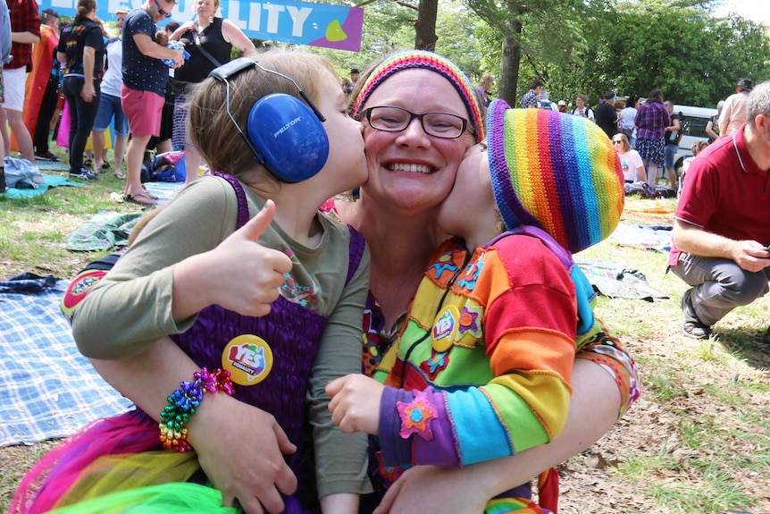 A woman is kissed by her two children.