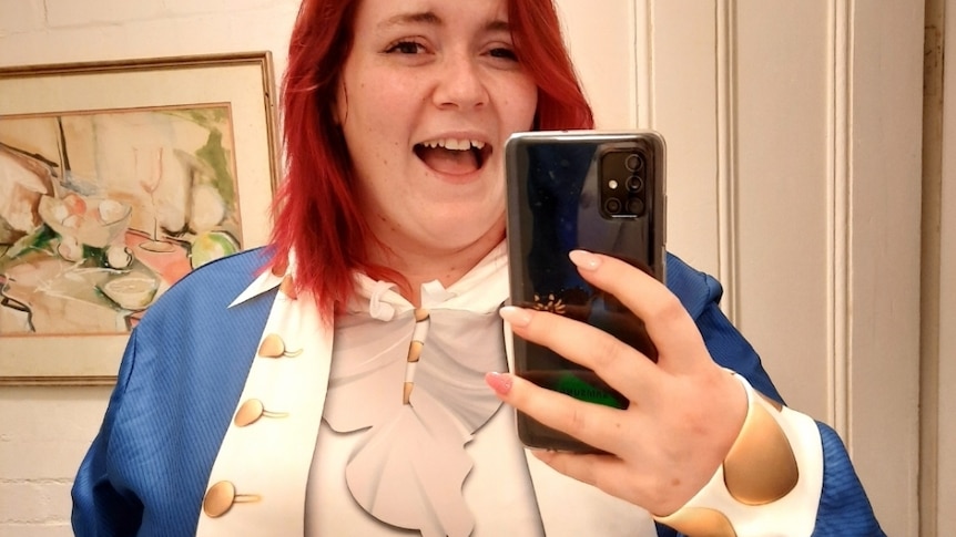A young woman with red hair, wearing a Hamilton-inspired costume poses in a mirror selfie.