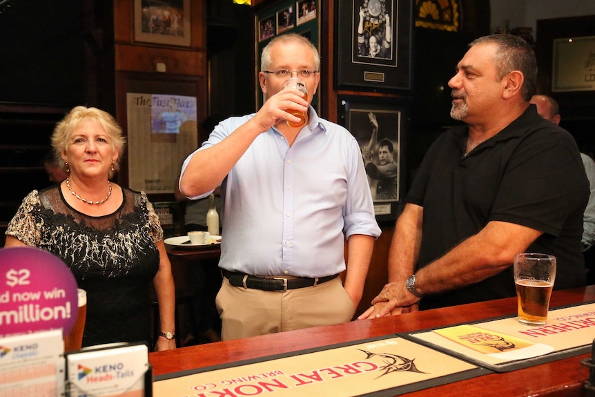 Scott Morrison drinks a beer as Michelle Landry stands alongside him inside a pub