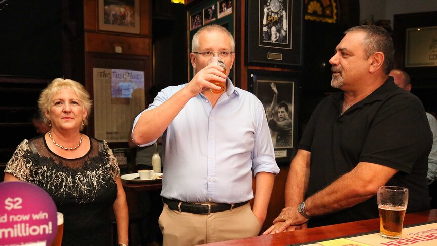 Scott Morrison drinks a beer as Michelle Landry stands alongside him inside a pub