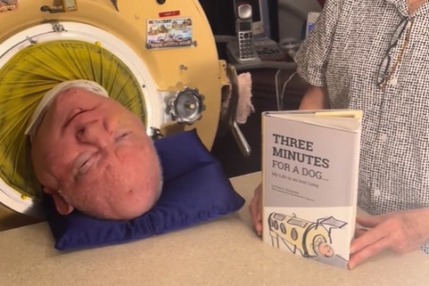 Paul Alexander in his iron lung with his memoir next to him as he talks about it