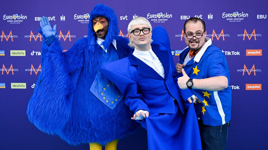 Joost Klein members, one in a blue bird costume, one in a blue suit and the other in an EU flag shirt
