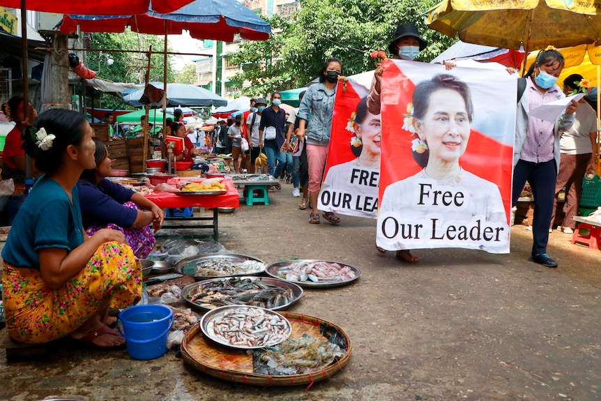 Anti-coup protesters walk through a market with images of ousted Myanmar leader Aung San Suu Kyi.