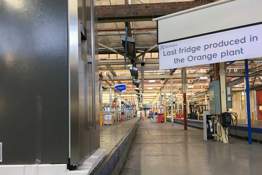A fridge sits at the end of a production line with a sign saying last fridge produced in the Orange plant